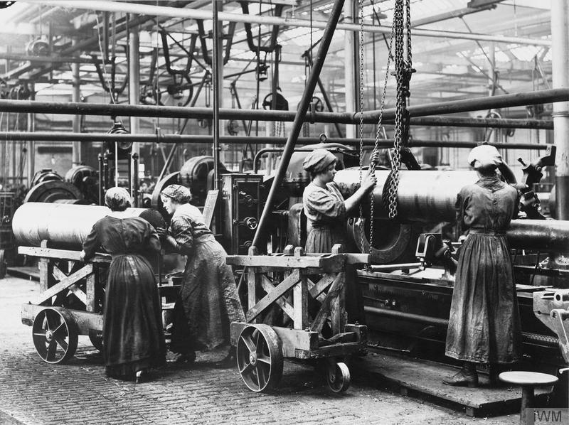 Female munition workers transporting large shells in a factory. © IWM (Q 110230)
